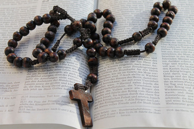 Foto di un rosario con una croce di legno sopra una bibbia aperta