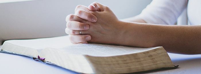Immagine di una persona con le mani giunte che prega su di una bibbia