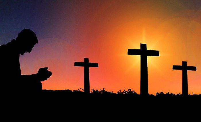 Immagine di una persona che prega davanti a tre croci.
